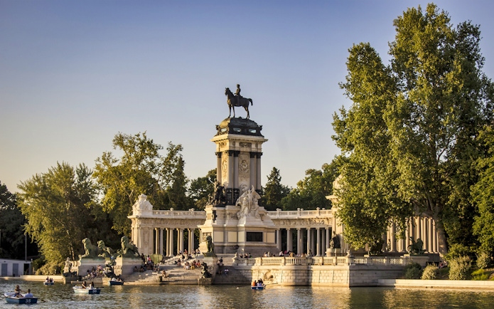 Monument to Alfonso XII at El Retiro Park, Madrid, with people boating nearby.