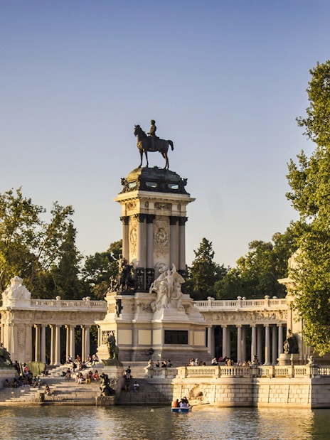 Monument to Alfonso XII at El Retiro Park, Madrid, with people boating nearby.