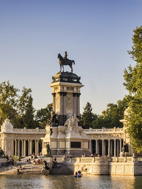 Monument to Alfonso XII at El Retiro Park, Madrid, with people boating nearby.