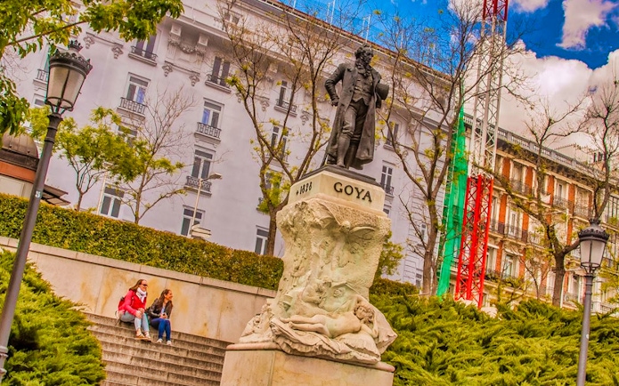 Goya statue near Prado Museum, Madrid, with visitors seated on steps.