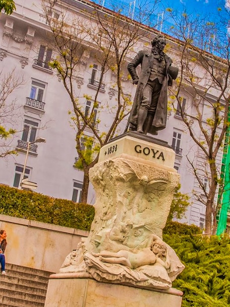 Goya statue near Prado Museum, Madrid, with visitors seated on steps.