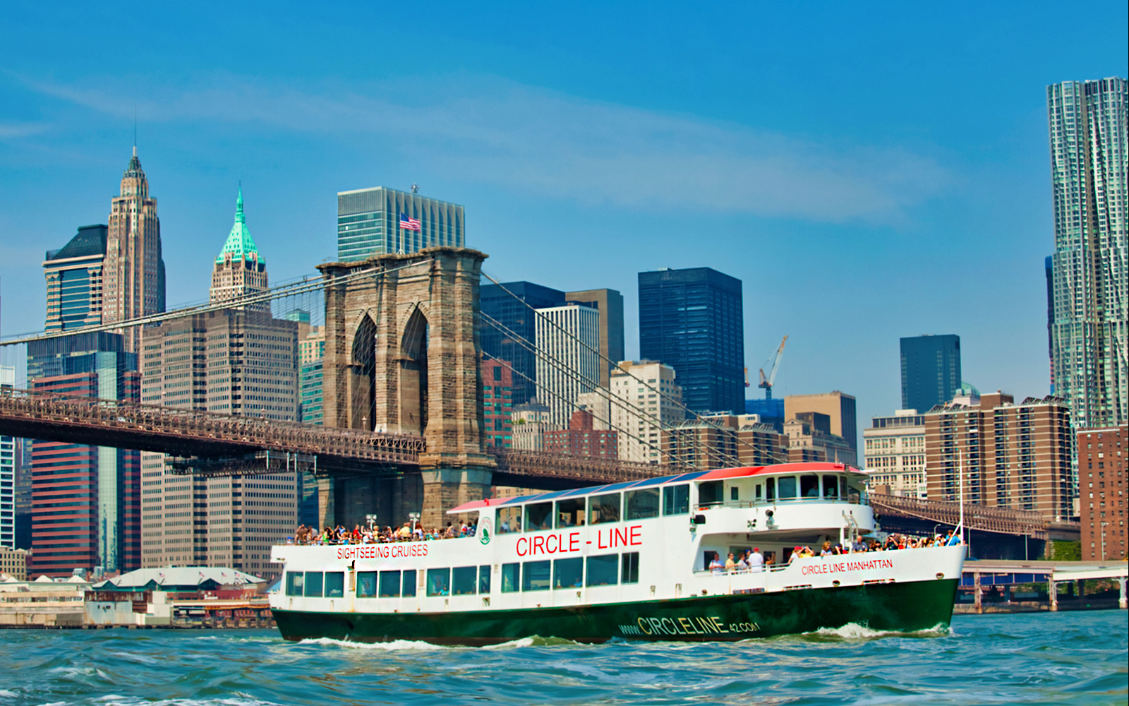 Sightseeing cruise near Brooklyn Bridge with New York City skyline.