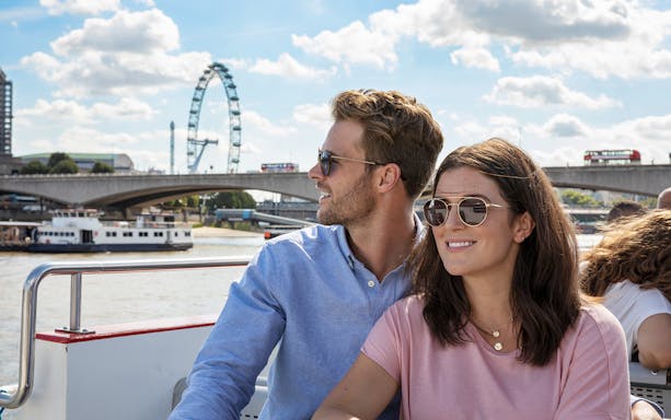 Couple enjoying a boat tour on the Thames with the London Eye in the background.