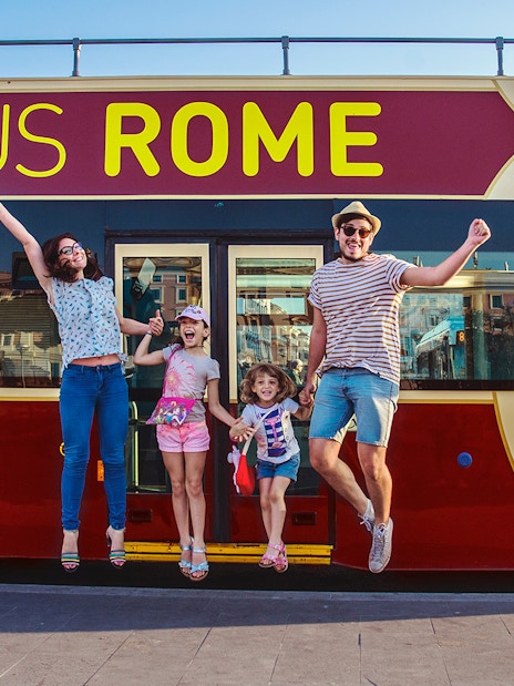 Family jumping in front of a Big Bus Rome tour bus, enjoying a hop-on hop-off experience.