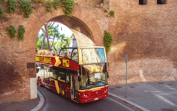 Open-top Big Bus tour passing through ancient Roman arch in Rome.