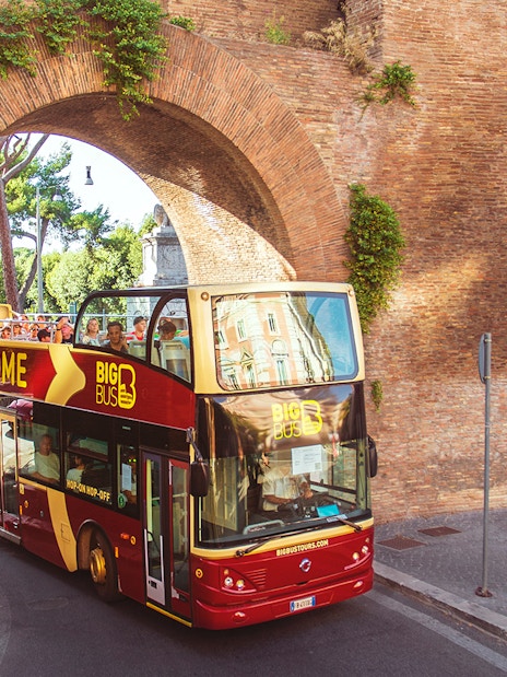 Open-top Big Bus tour passing through ancient Roman arch in Rome.