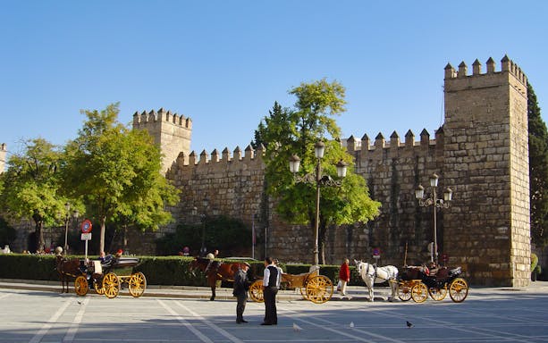 Alcázar of Seville entrance with horse-drawn carriages in foreground.
