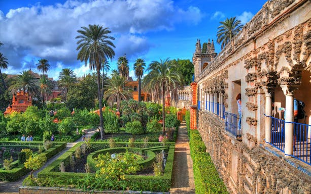 Alcázar gardens with palm trees and historic architecture in Seville, Spain.