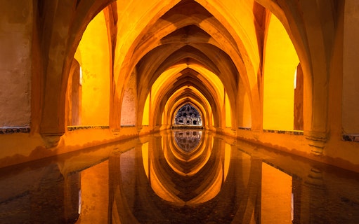Alcázar of Seville underground baths with arched ceilings and reflections in water.
