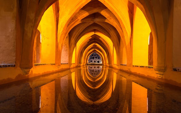 Alcázar of Seville underground baths with arched ceilings and reflections in water.