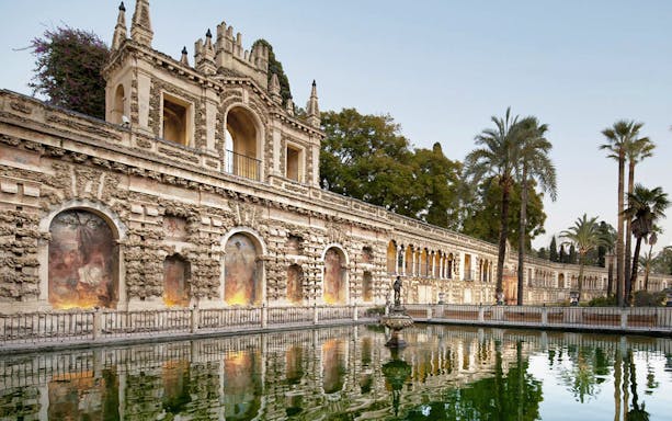 Alcázar of Seville exterior with reflecting pool and ornate architecture.
