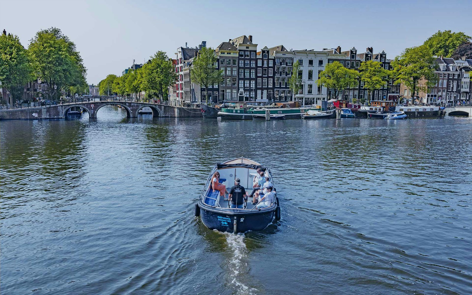 Boat cruising on Amsterdam canal with historic buildings and bridge in view.