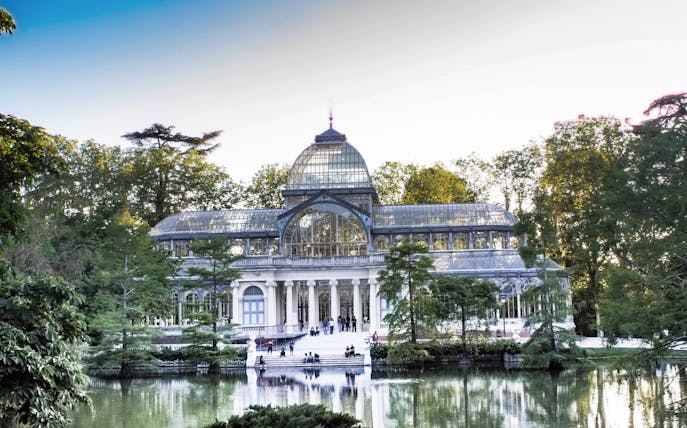 Crystal Palace in El Retiro Park, Madrid, surrounded by trees and reflecting pond.