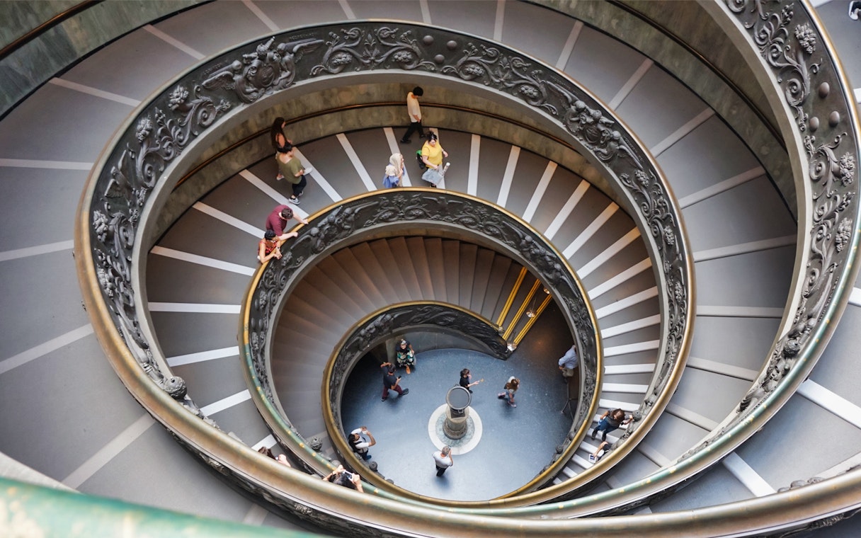 Spiral staircase in Vatican Museums, Rome, with visitors descending.