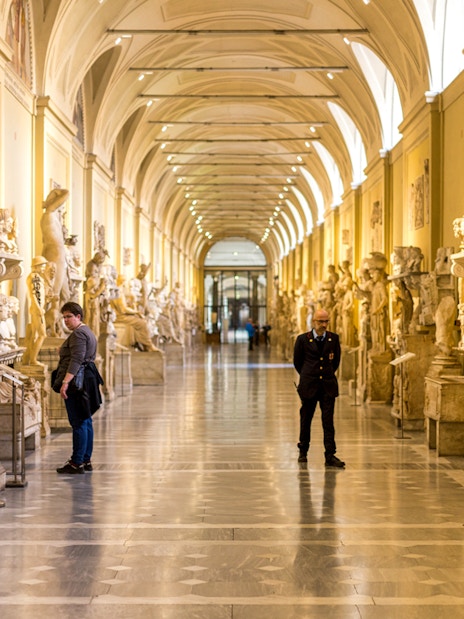 Vatican Museums hallway with classical sculptures and visitors exploring exhibits.