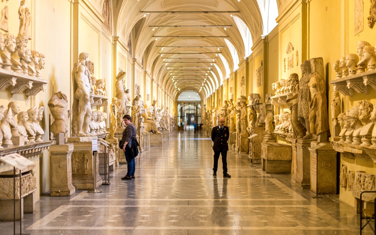 Vatican Museums hallway with classical sculptures and visitors exploring exhibits.