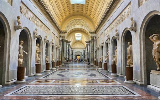 Vatican Museums hallway with classical sculptures and ornate ceiling.