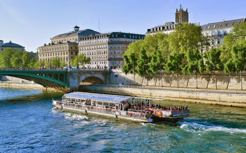Seine River cruise boat passing under a bridge in Paris with historic buildings in view.