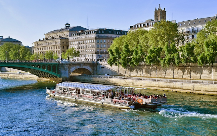 Seine River cruise boat passing under a bridge in Paris with historic buildings in view.