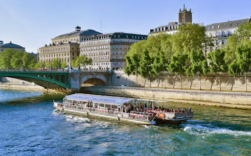 Seine River cruise boat passing under a bridge in Paris with historic buildings in view.