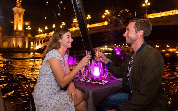 Couple toasting with champagne on a La Marina dinner cruise in Paris at night.