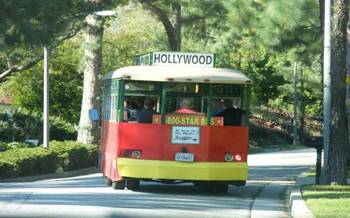 Hollywood trolley bus driving through tree-lined street.