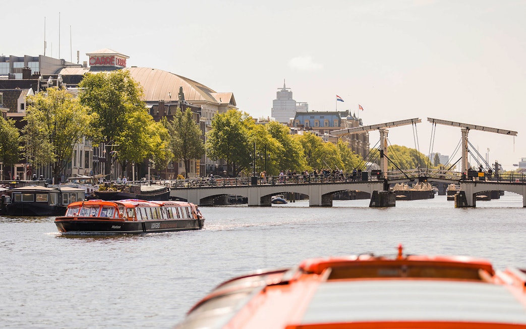 Canal cruise boat on Amsterdam's Amstel River near Magere Brug bridge.
