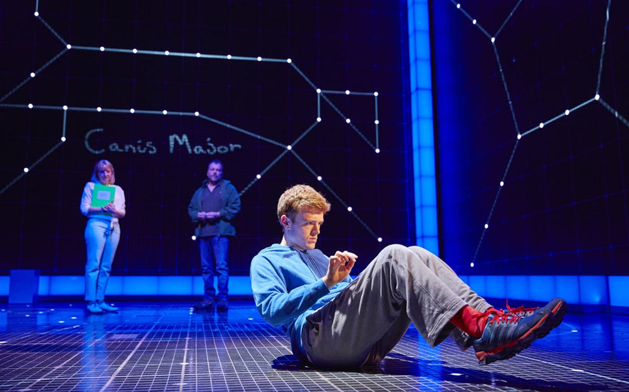 Young man on stage with constellation backdrop in "The Curious Incident of the Dog in the Night-Time" play.