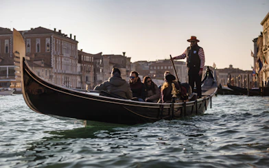 Gondola ride on Venice canal with tourists and gondolier, historic buildings in background.