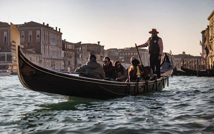 Gondola ride on Venice canal with tourists and gondolier, historic buildings in background.