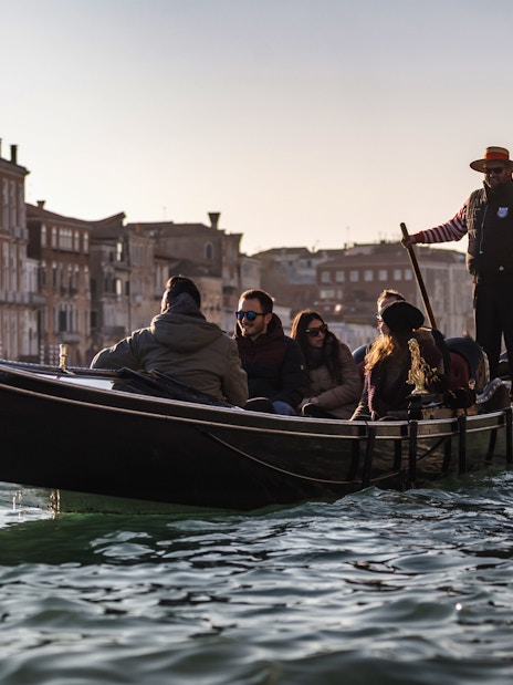 Gondola ride on Venice canal with tourists and gondolier, historic buildings in background.