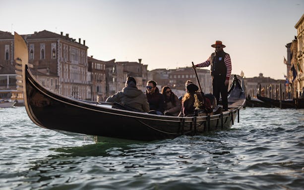 Gondola ride on Venice canal with tourists and gondolier, historic buildings in background.