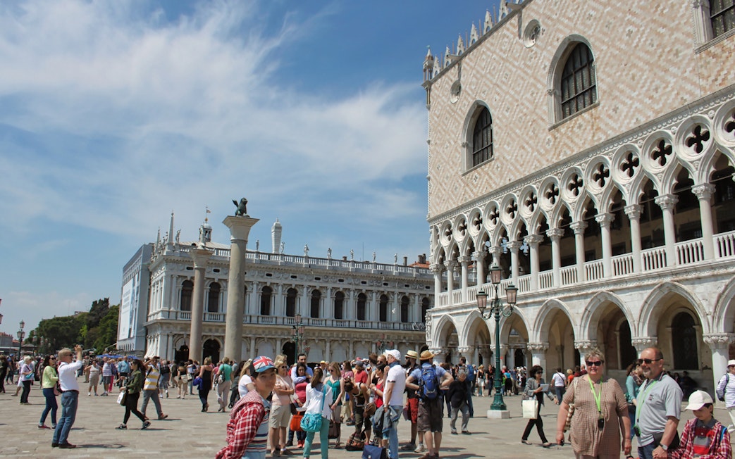 Crowd outside Doge's Palace in Venice with guidebooks, near St. Mark's Square.