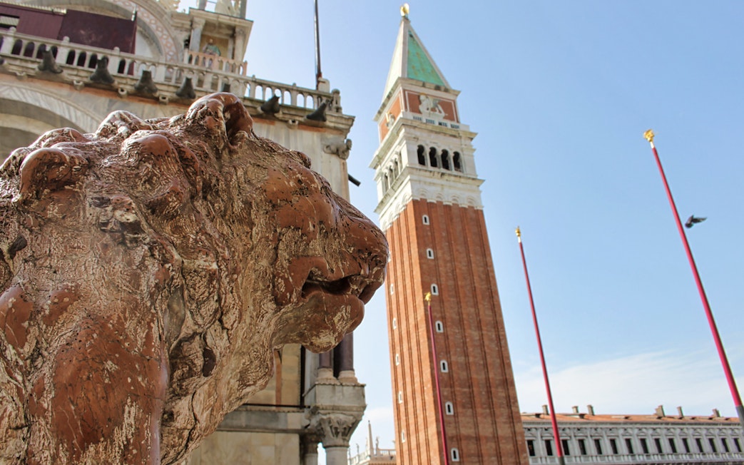 Lion statue near Doge's Palace with St. Mark's Campanile in Venice, Italy.