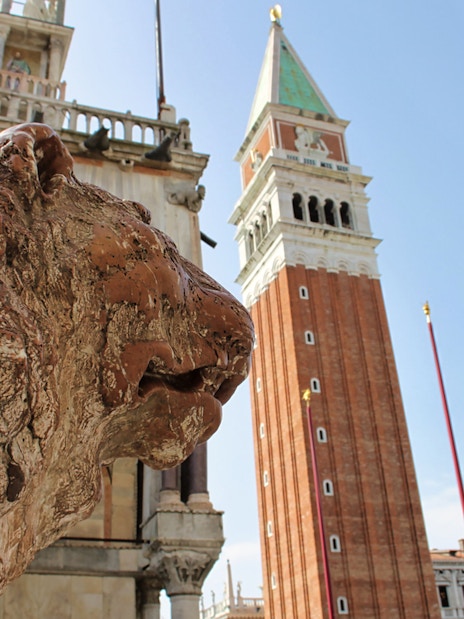 Lion statue near Doge's Palace with St. Mark's Campanile in Venice, Italy.
