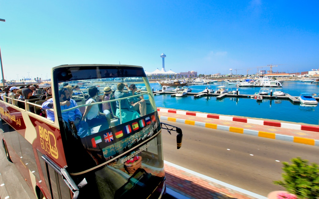Open-top bus with tourists on Abu Dhabi waterfront during Big Bus sightseeing tour.