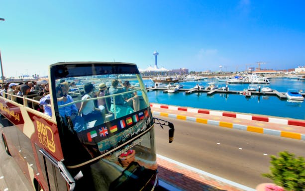 Open-top bus with tourists on Abu Dhabi waterfront during Big Bus sightseeing tour.