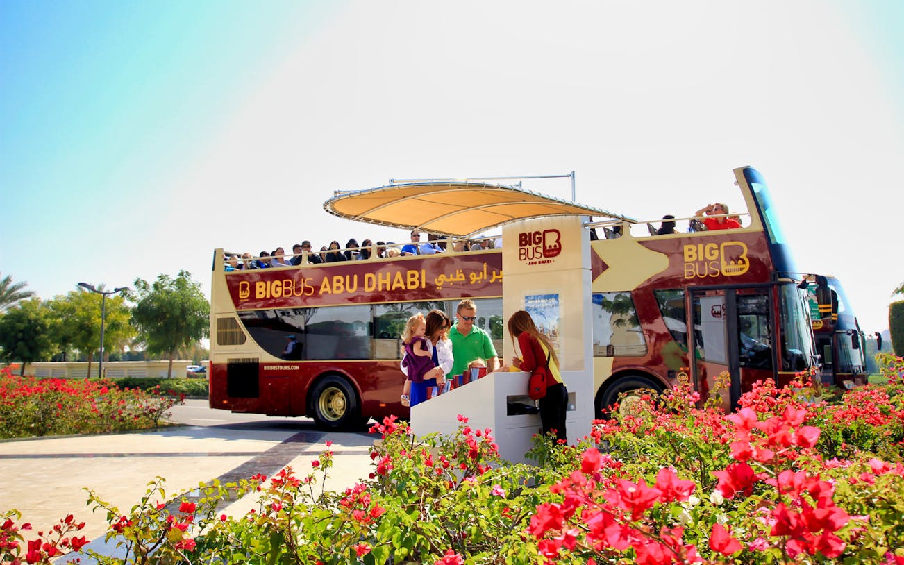 Big Bus Abu Dhabi tour bus with passengers boarding near vibrant flowers.