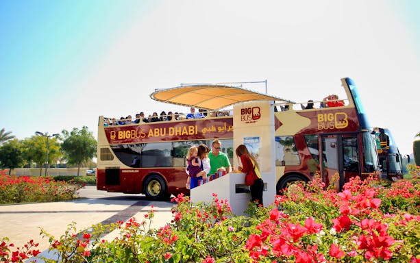 Big Bus Abu Dhabi tour bus with passengers boarding near vibrant flowers.