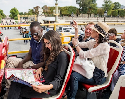 Tourists on Big Bus Paris tour, viewing map, with Eiffel Tower and Seine River in background.