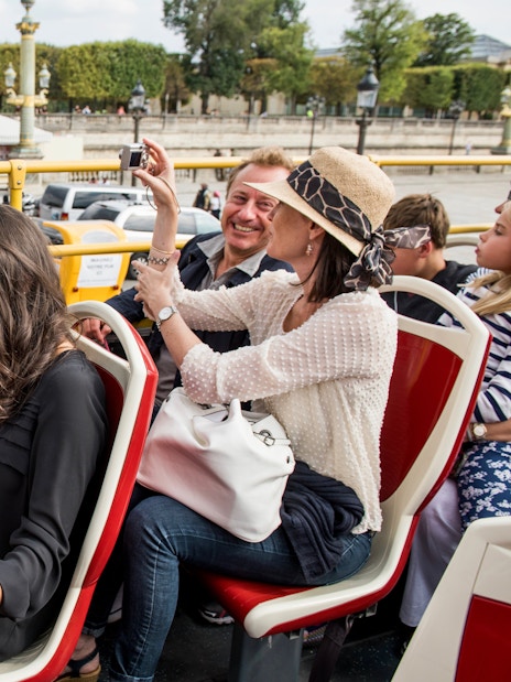 Tourists on Big Bus Paris tour, viewing map, with Eiffel Tower and Seine River in background.
