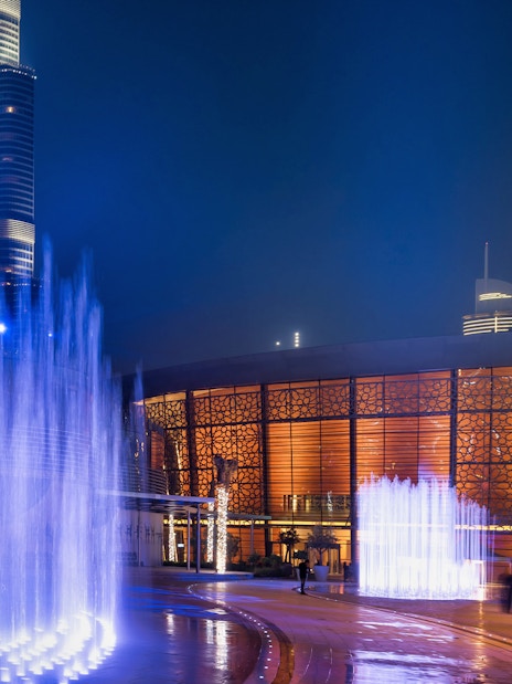 Dubai Opera House illuminated at night with nearby fountains.