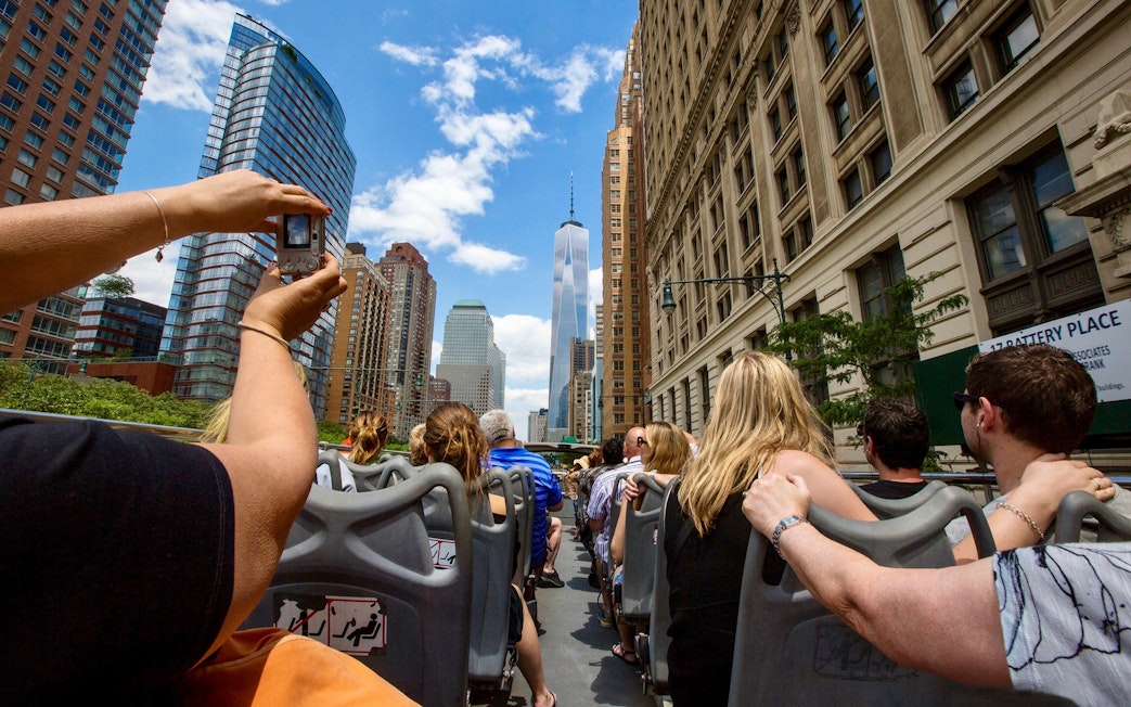 Open-top bus tour in New York City with view of skyscrapers and tourists.