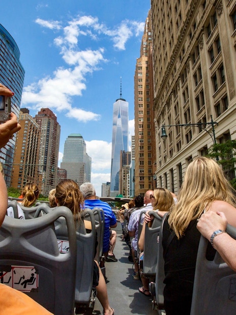 Open-top bus tour in New York City with view of skyscrapers and tourists.
