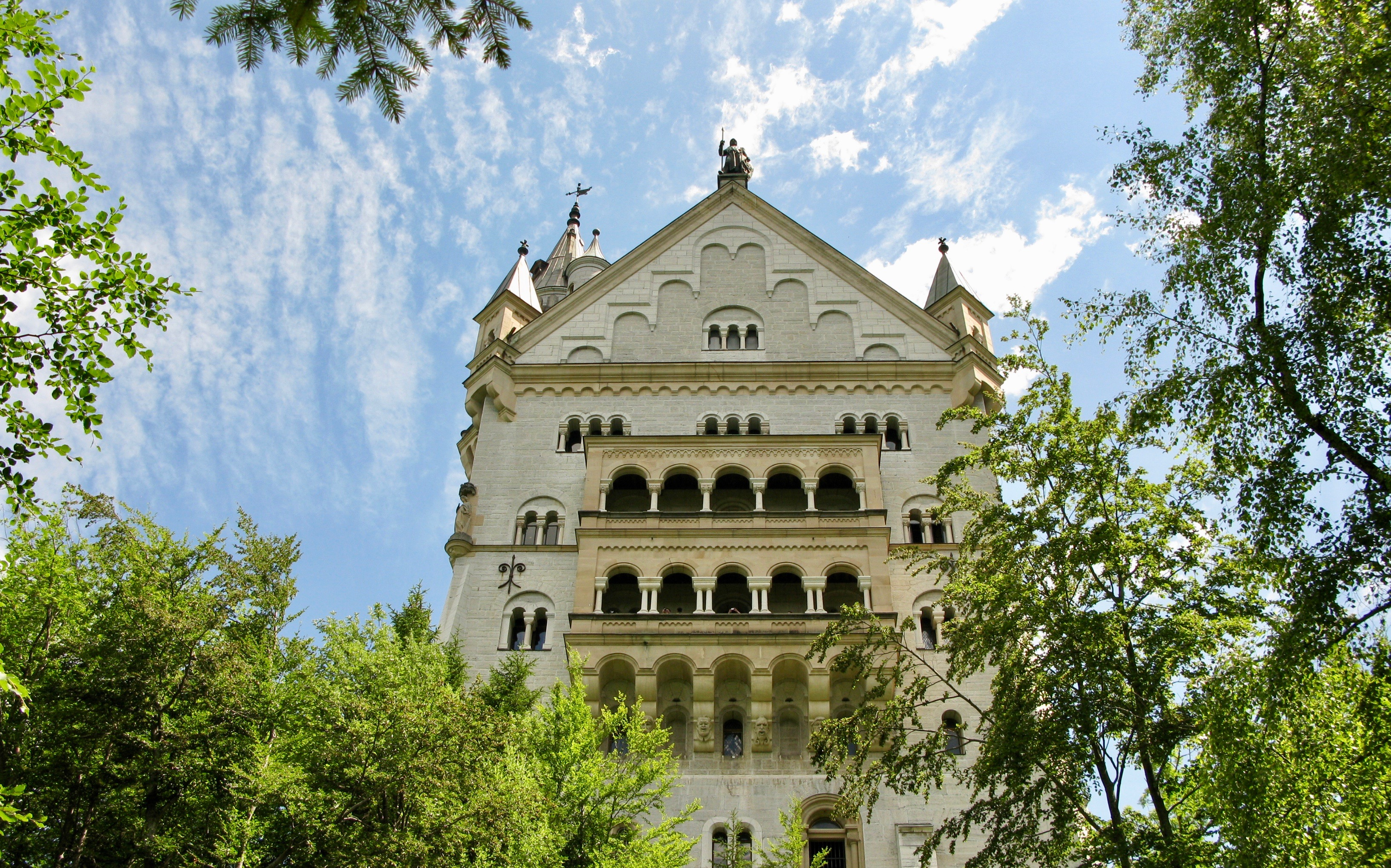 Neuschwanstein Castle facade surrounded by trees, viewed from below, Bavaria, Germany.