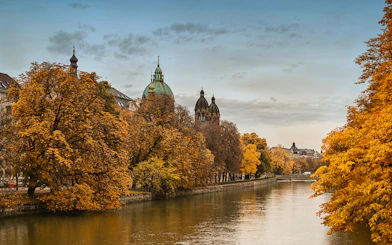 Munich river view with autumn trees and historic buildings, part of Neuschwanstein tour.
