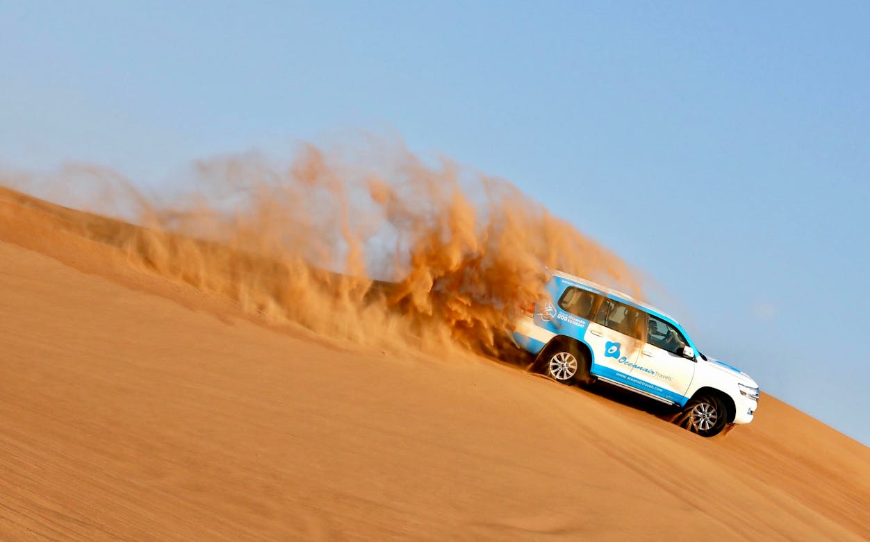 SUV driving through sand dunes during morning desert safari.
