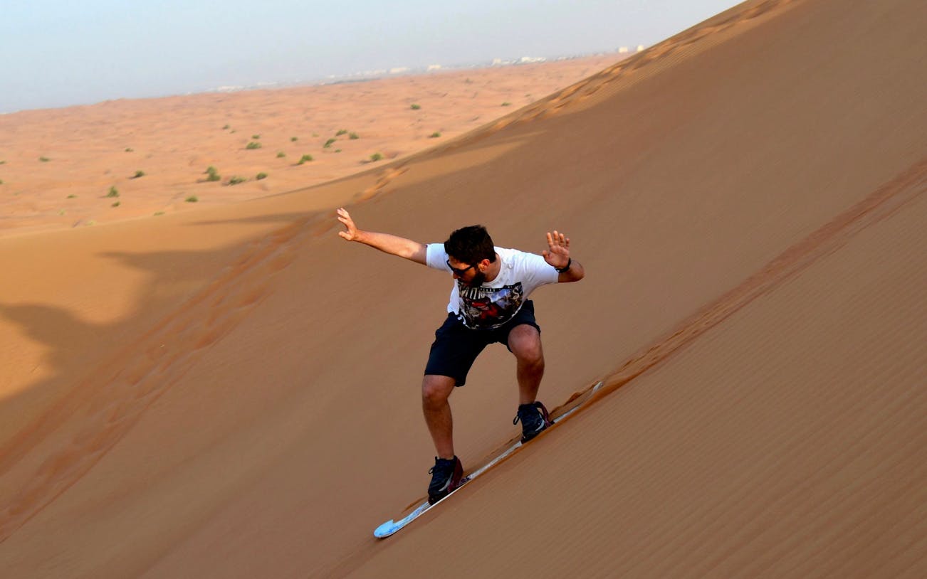Sandboarding down a dune during a morning desert safari.