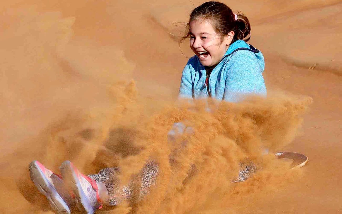 Child enjoying sandboarding during a morning desert safari.