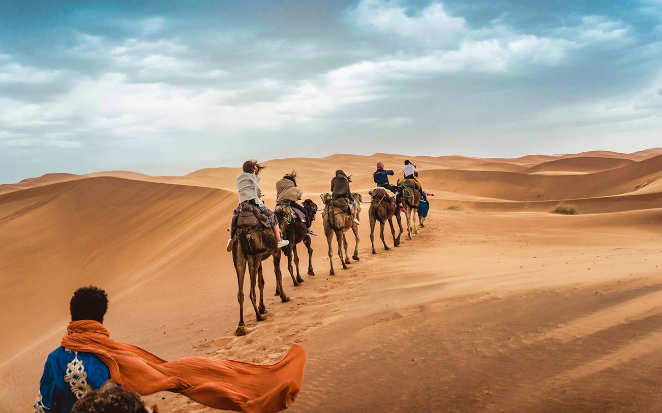 Tourists enjoying a Sunset Camel Trek with BBQ Dinner in the Dubai desert